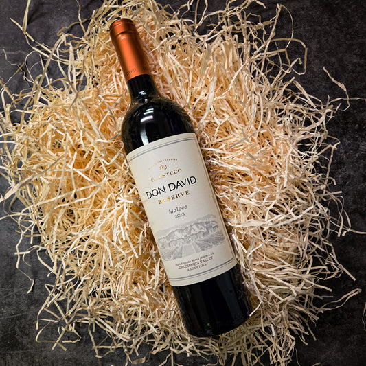Bottle of Don David Reserve wine on a bed of straw with a dark background
